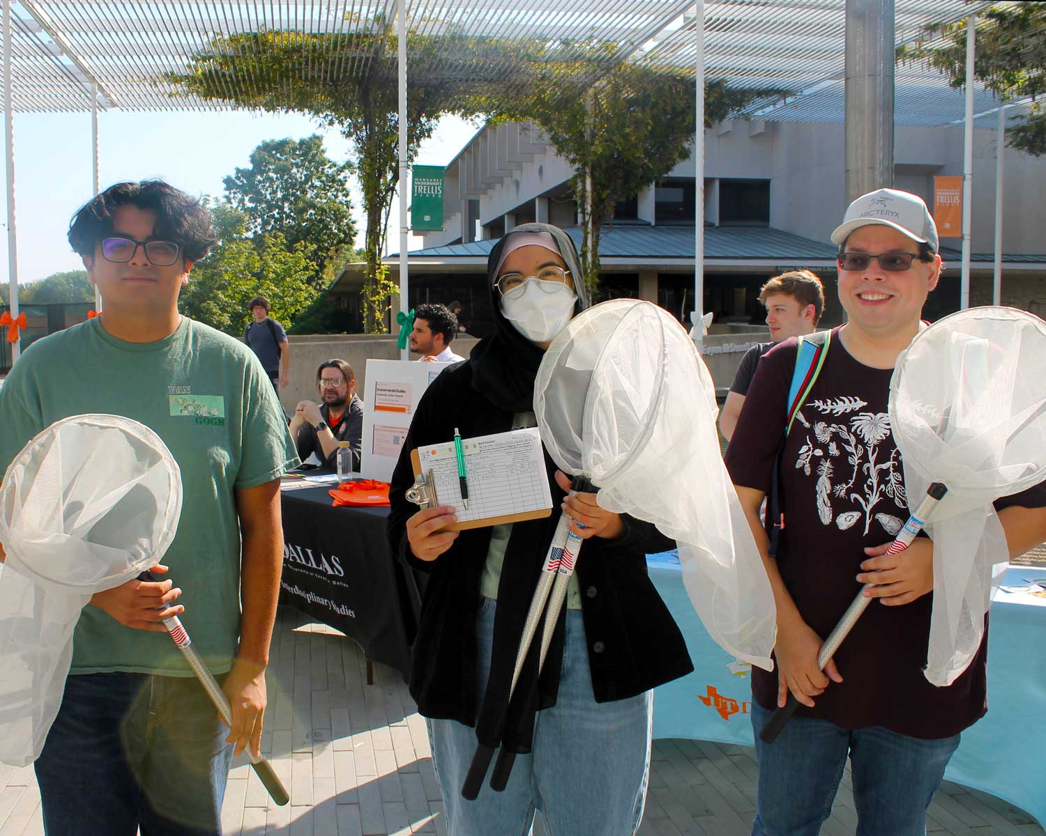 Three students holding butterfly nets while standing in the middle of Margaret McDermott Trellis Plaza on the UT Dallas campus.