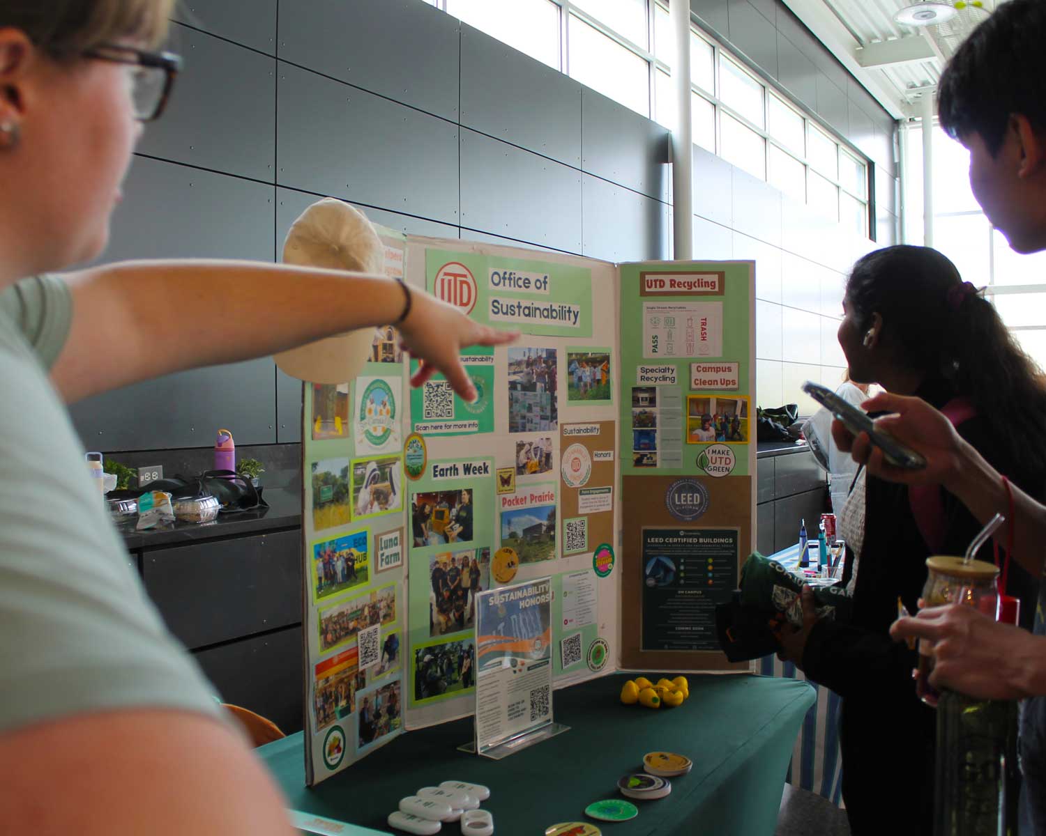 An Eco Rep at a table display explaining UTD Sustainability to a pair of students.