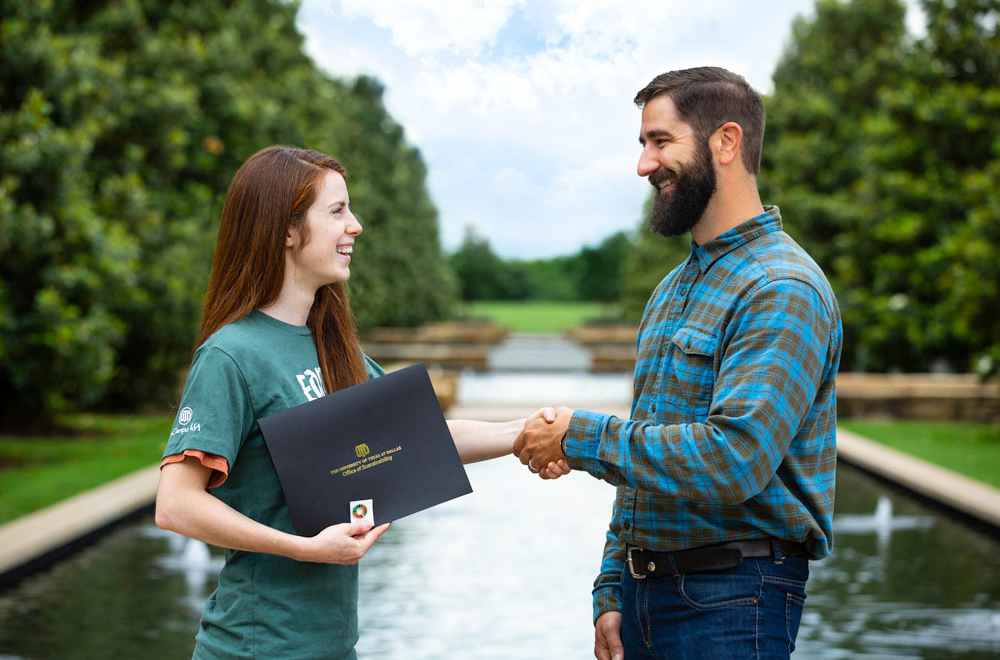 A student shakes hands with the Associate Director of Energy Conservation & Sustainability in front of the University’s reflacting pools while receiving the Sustainability Service Honor.