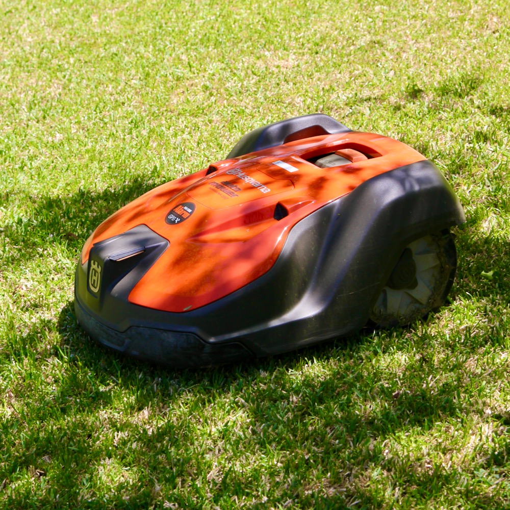 A squat orange and grey machine on wheels cutting a lawn by itself.