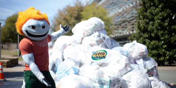 Campus Race to Zero Waste. University mascot Temoc stands before a pile of filled recycling bags.
