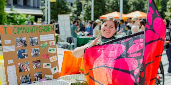 Earth Week Kicks Off April 18th. A volunteer at the UTD Community Garden Table during Earth Week, displaying a giant butterfly wing.