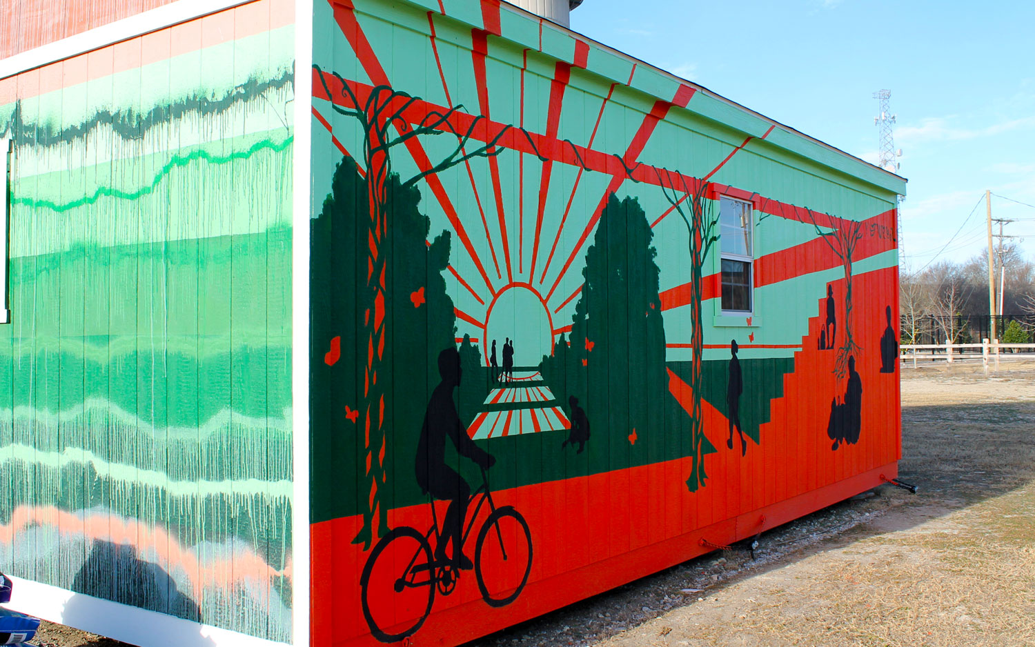 The side of a single-story gabled-roof building, painted with an abstract mural depicting the Trellis Plaza in Margaret McDermott Mall at UT Dallas.