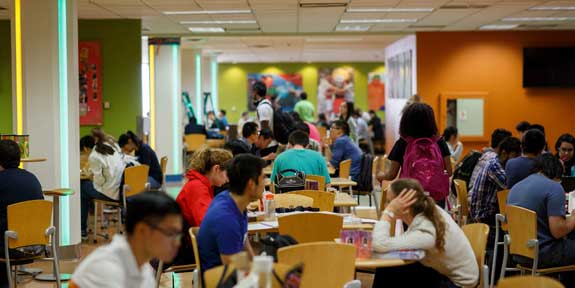 Dine Green at Dining Hall West. A large room filled with students seated at tables, eating.