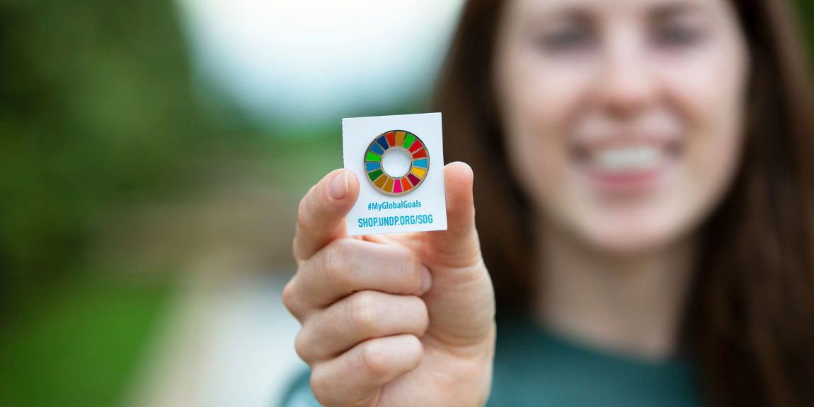 A person holding up an enamel pin of the symbol for the United Nations Sustainable Development Goals.