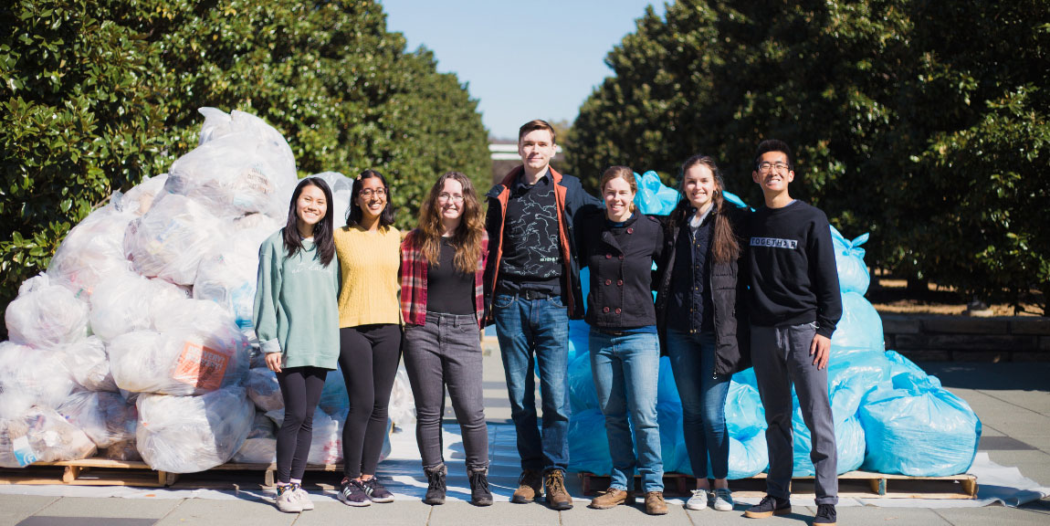 A group of students standing in front of a large pile of filled recycling bags.