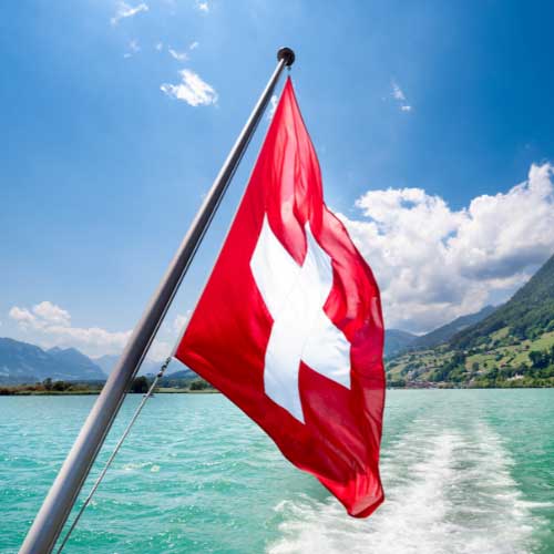A Swiss flag mounted off the back of a boat on a mountain lake.