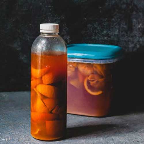 A bottle and a small container tub, both filled with fruit peels and an orange liquid.