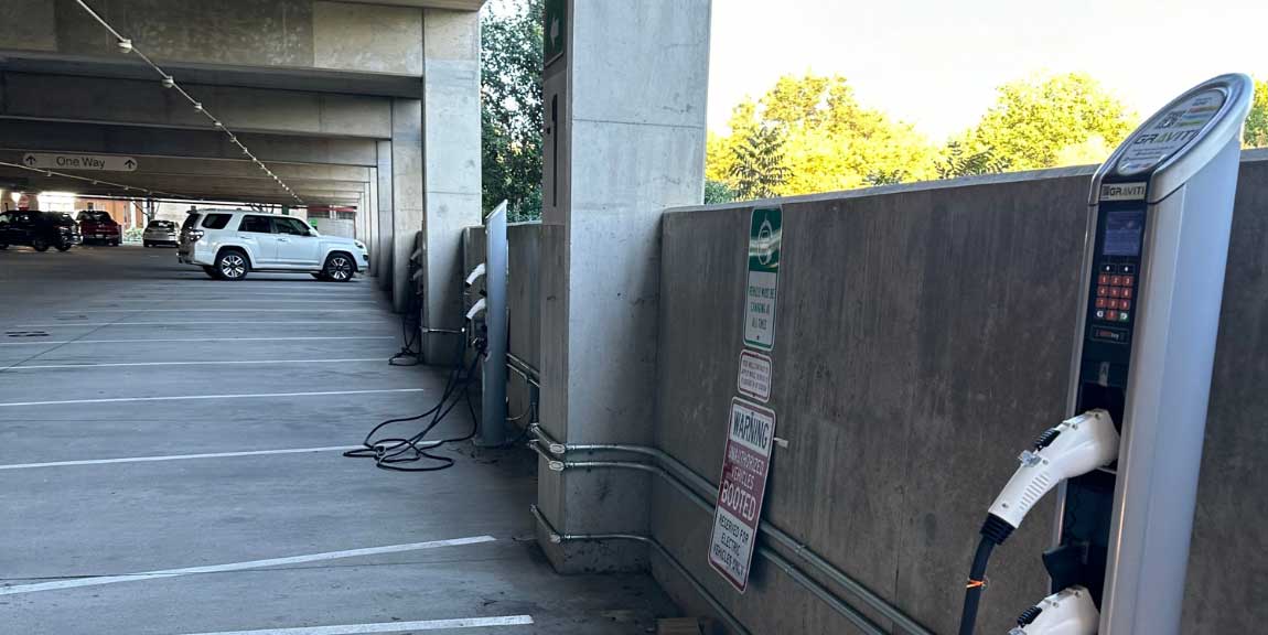 Three electric vehicle chargers standing in a row along a wall inside a parking garage.