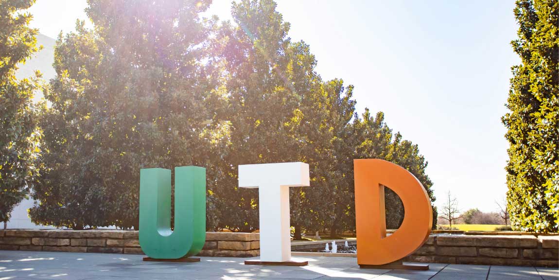 Three large letters, U-T-D, standing upright in the middle of Margaret McDermott Mall on the UTD campus.