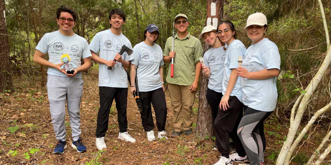 A groups of students in the woods holding tools.