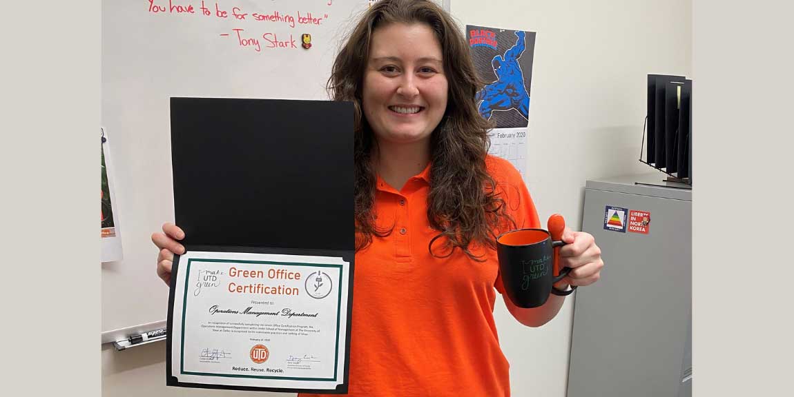 A staff member holding a green office certification and mug.