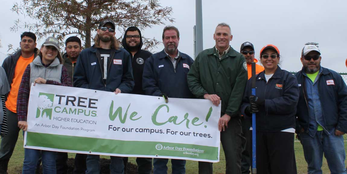 A group of UT Dallas Eco Reps and landscape workers hold up a “Tree Campus Higher Education” banner.