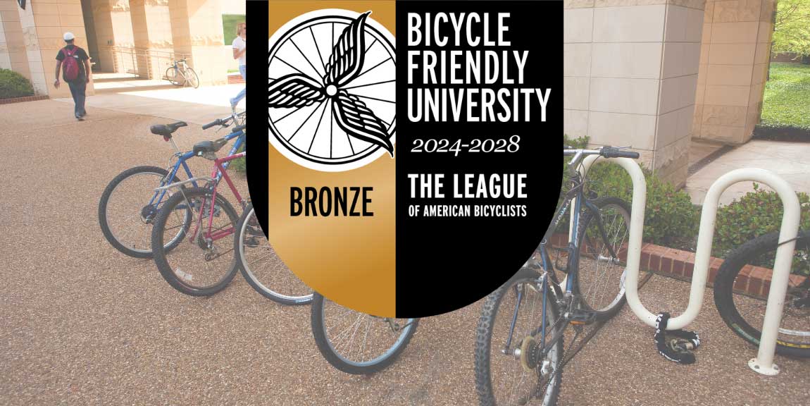 The bronze “Bicycle Friendly University” badge from the League of American Bicyclists, floating over a photo of one of the many bike racks on the UT Dallas campus.