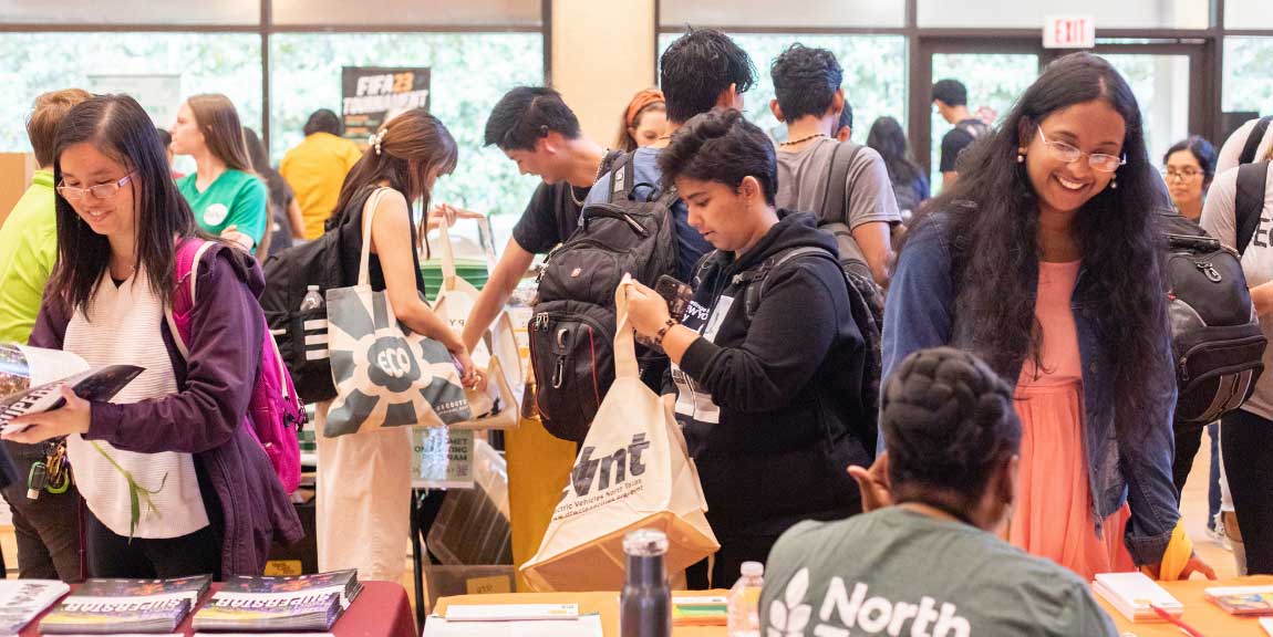 Students move between rows of tables set up in the UTD Student Union, each covered with stacks of literature and staffed by a member of a different organization.