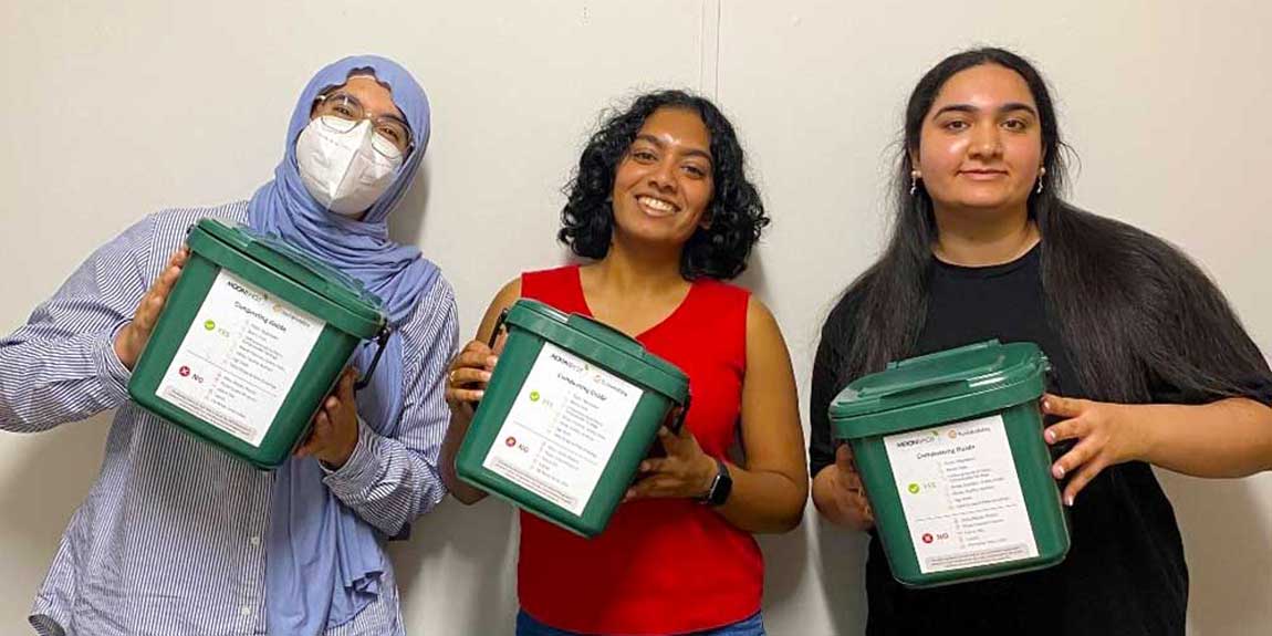 Three students holding up composting bins.