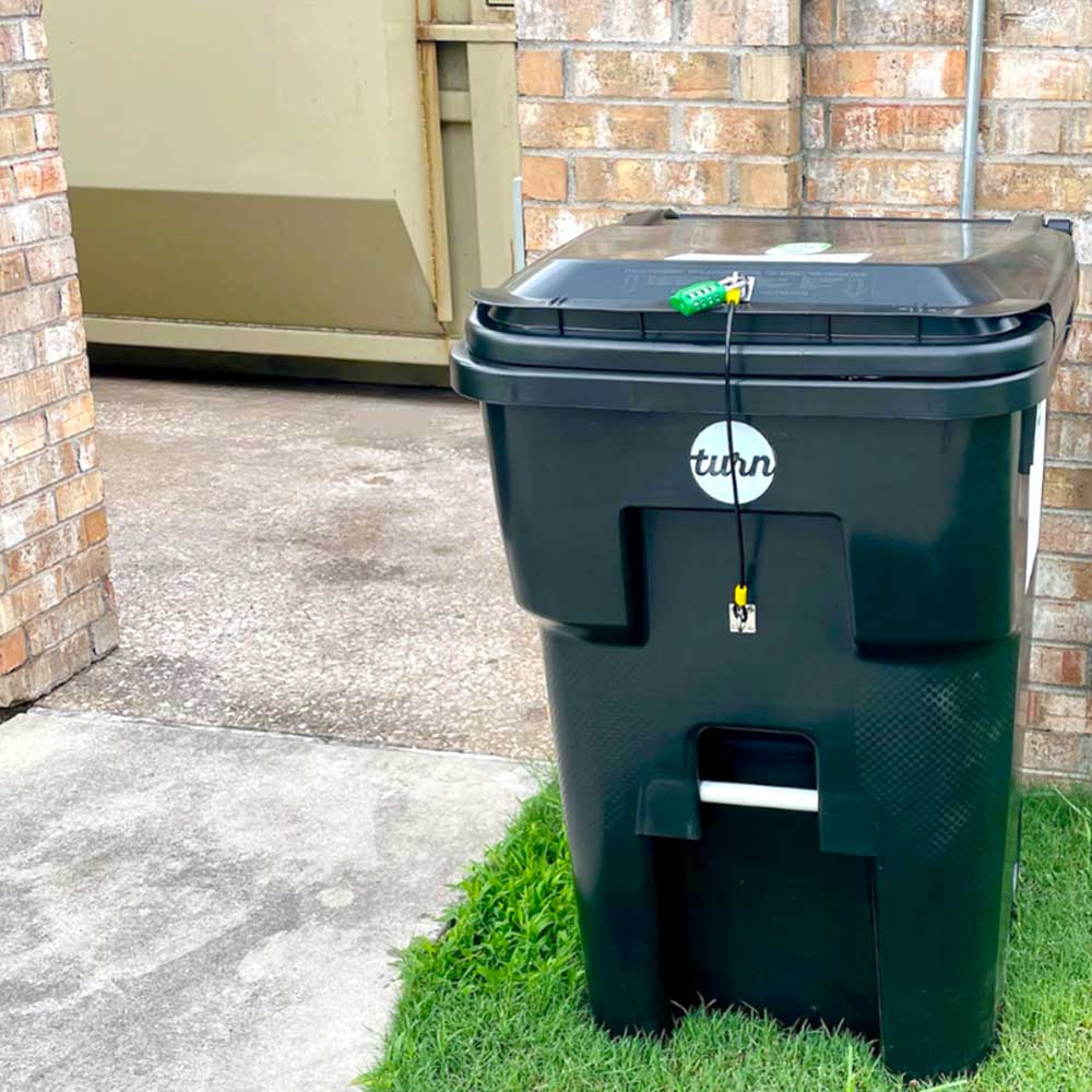 A large composting bin standing outside a building.