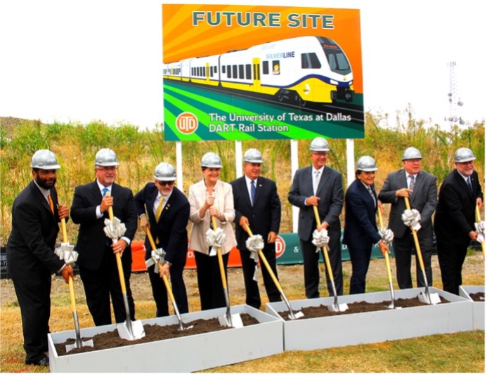 UTD administrators and city officials in hardhats break ground on a new light rail station.