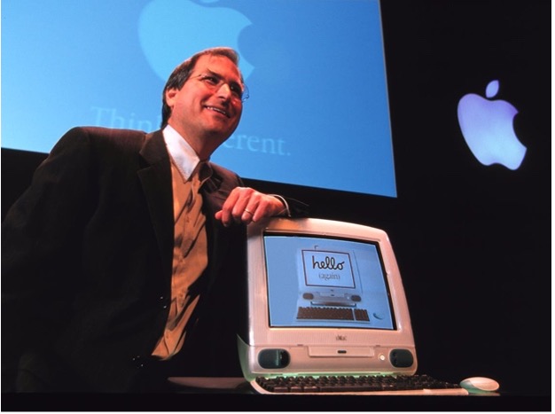 A man stands next to the original Apple iMac.