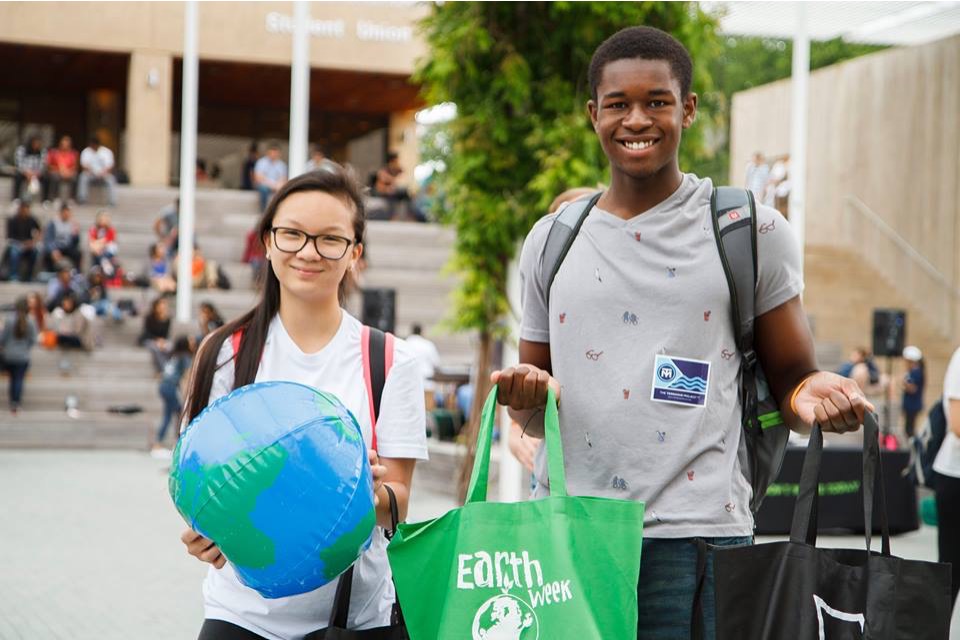 Students holding Earth Week tote bags and inflatable globes.