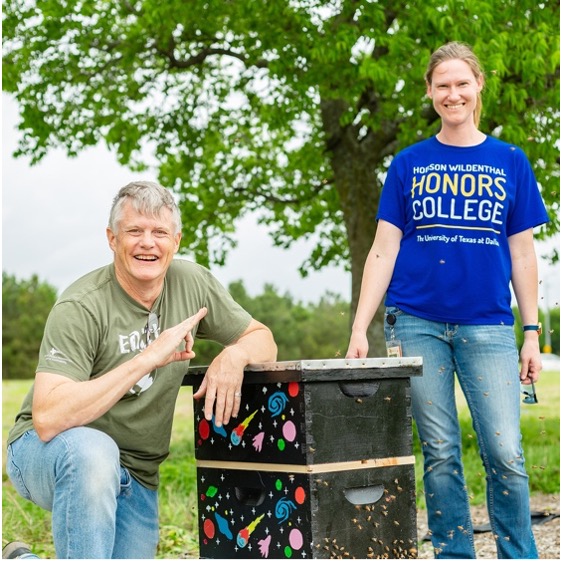 Two people standing next to a bee hive painted with a night sky pattern.