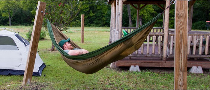 A man sleeping in a hammock next to a tent.