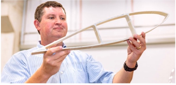 A researcher holds up a model of an airplane wing cross-section.