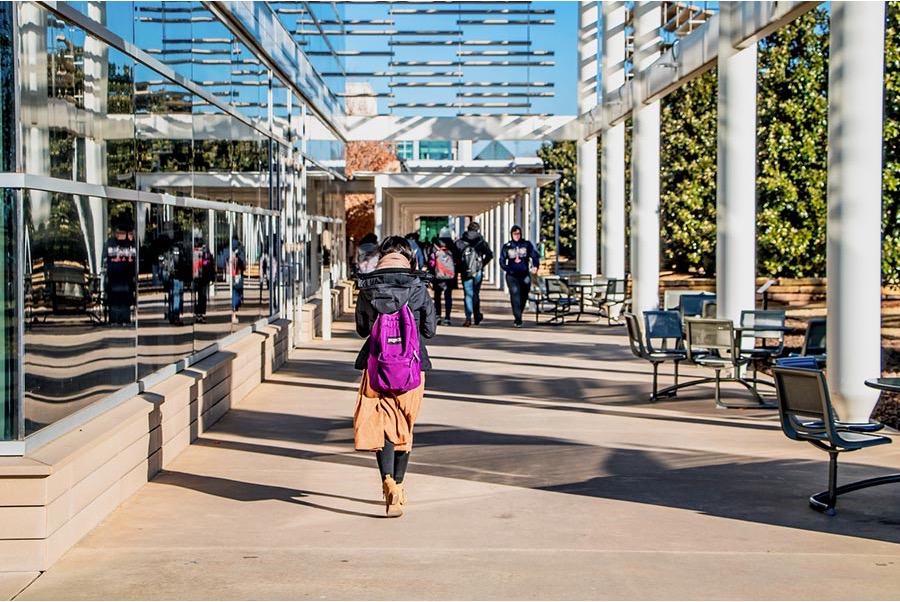 A student waking under the partial shade created by the front of the Student Services Center.